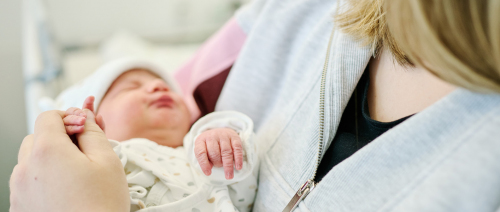 Mama im Patientenbett mit Neugeborenen unter dem Arm